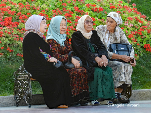 4 elderly ladies in head scarfs sitting on a bench