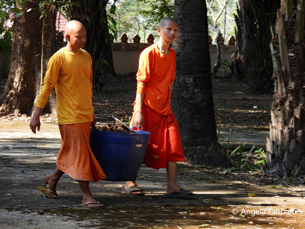 two monks carrying a bucket of firewood