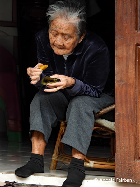 old woman eating sticky rice from palm leaf