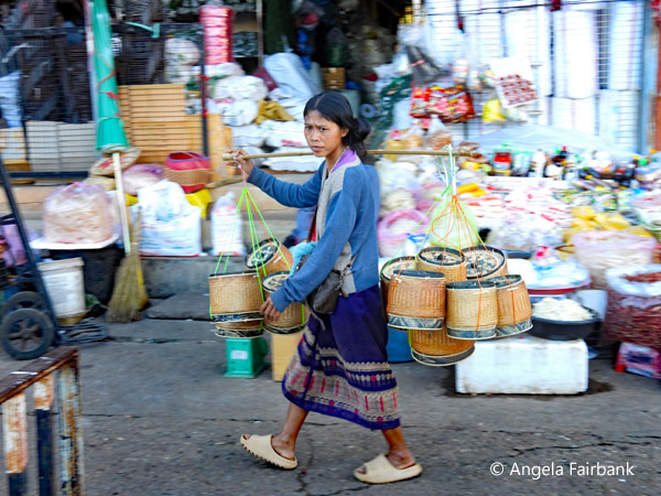 woman in market carrying pots on stick