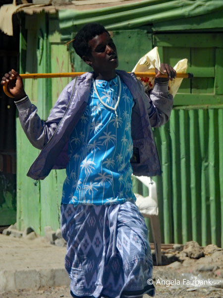 Dikhil boy in blue holding stick in both hnads