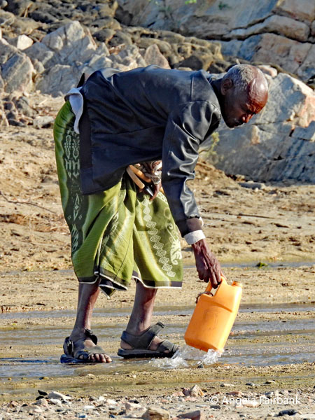 man collecting water in riverbed