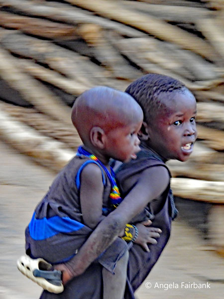 Lotuko girl runnign with brother on her back