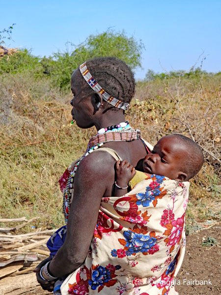 Toposa woman in headband carruing child on her back 1