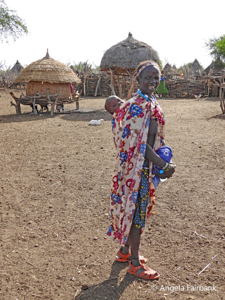 Toposa woman in headband carruing child on her back 2