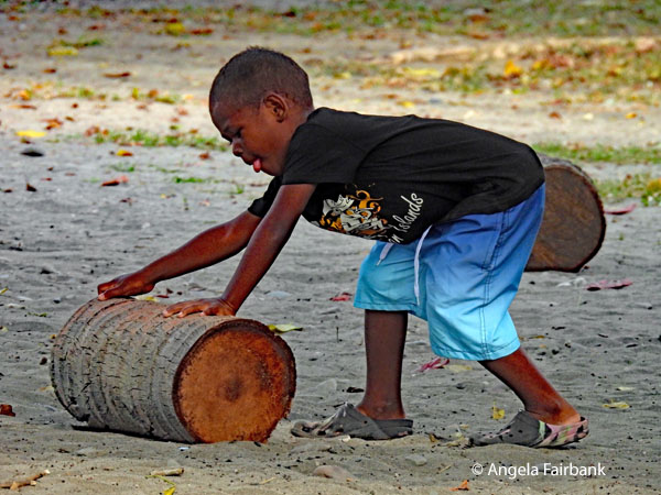 boy on land rolling a log with tongue sticking out