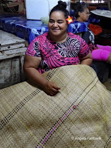 woman in market threading pink ribbon though reed mat