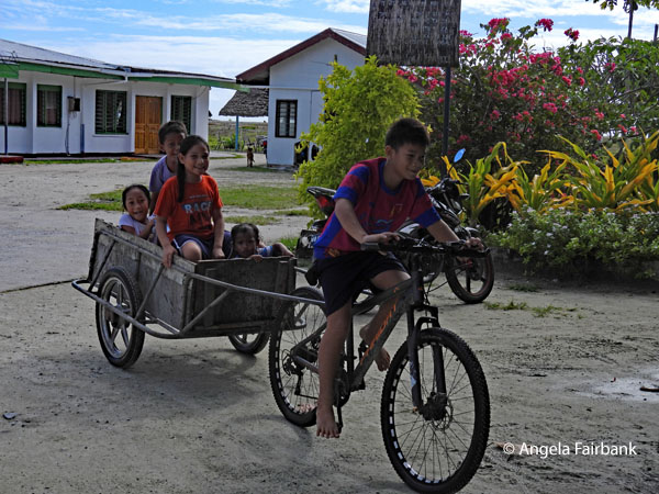 children in cart being pulling by boy on bicycle