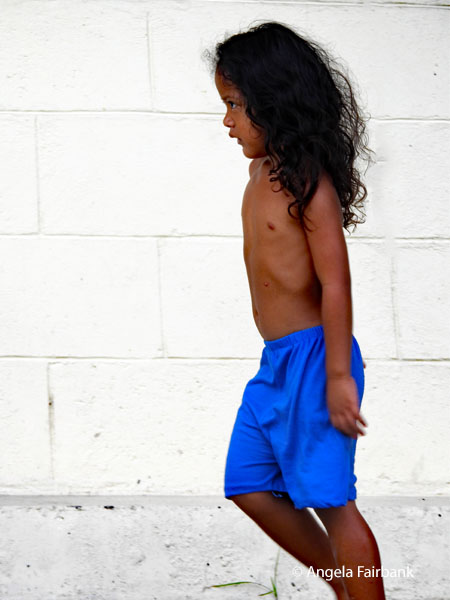 boy in shorts walking by a white brick wall