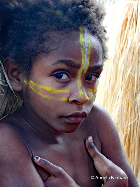 girl in yellow face paint with hands in armpits